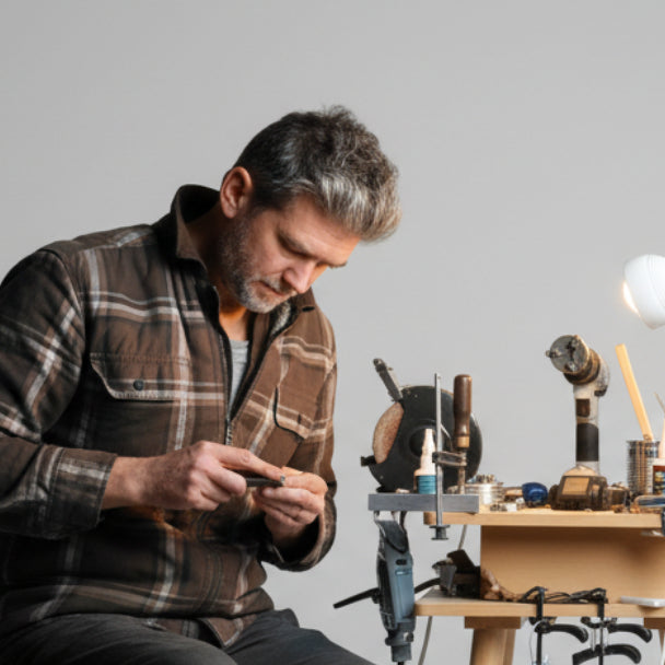 Person sitting at a workbench, surrounded by tools and equipment.