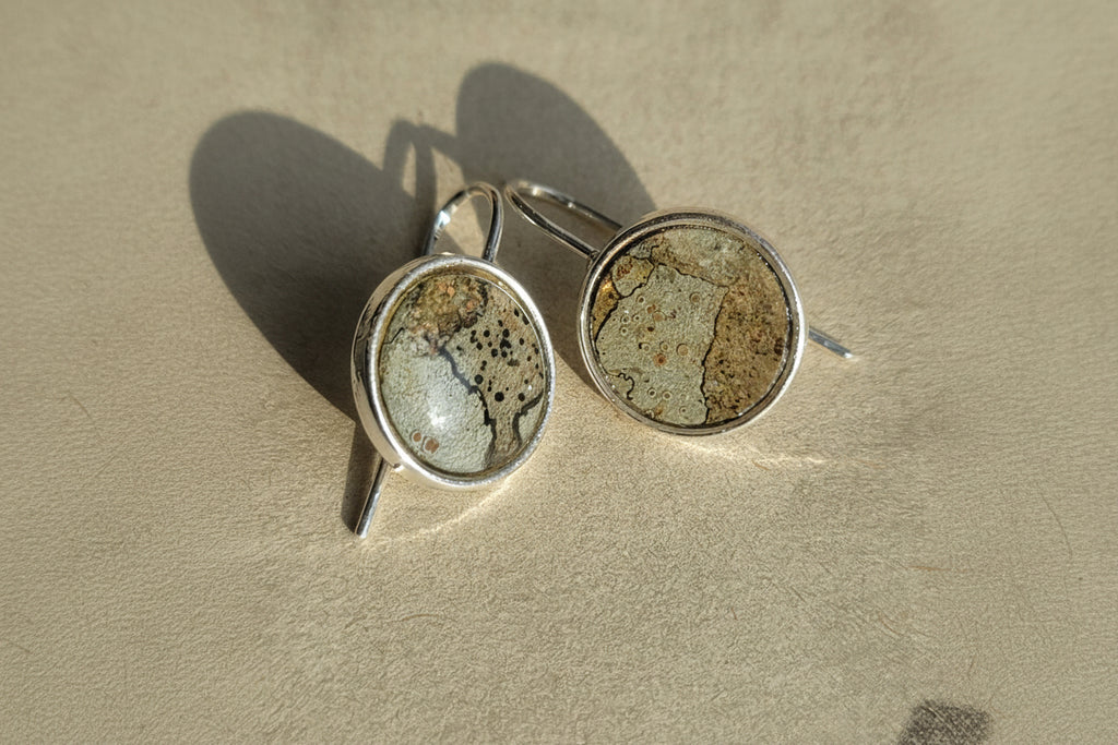 Two silver rings with stone-like inlays on a sandy surface