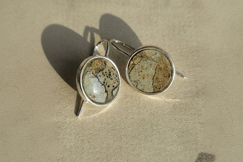 Two silver rings with stone-like inlays on a sandy surface