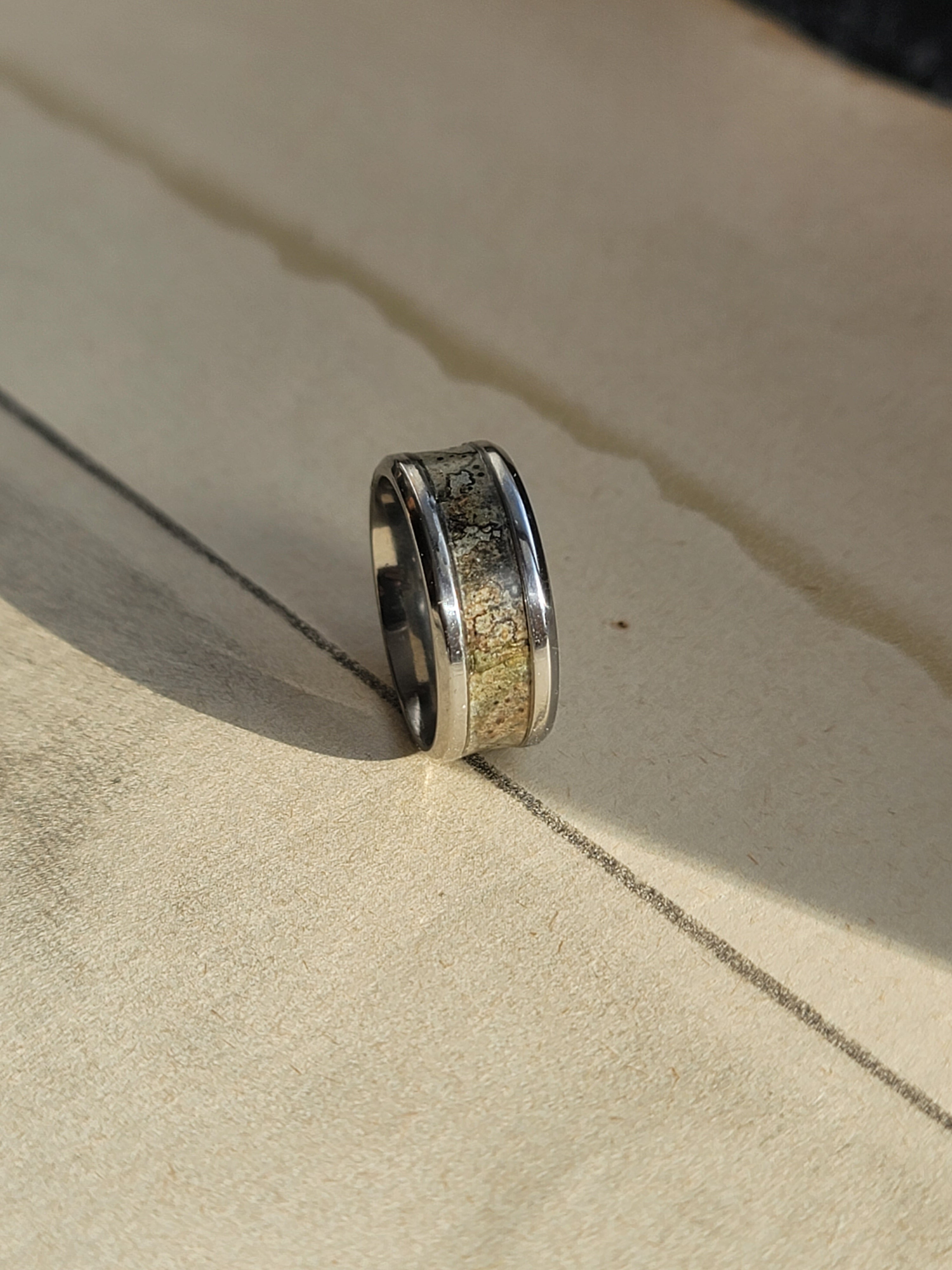 Steel ring with a textured band on a beige surface