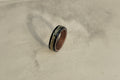 Wooden ring with black inlay on a textured beige surface