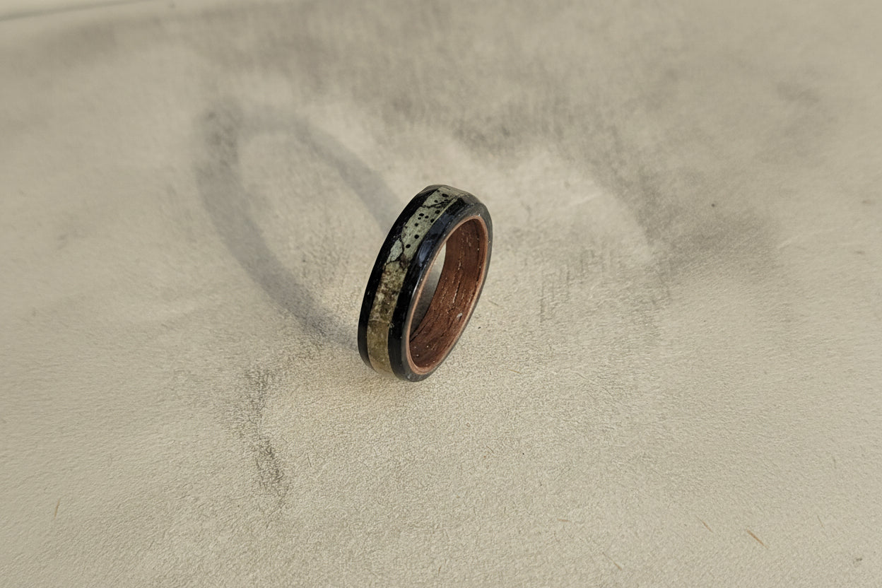 Wooden ring with black inlay on a textured beige surface