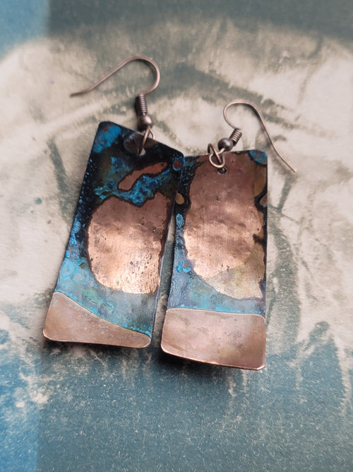 Pair of copper and blue enamel earrings on a textured surface
