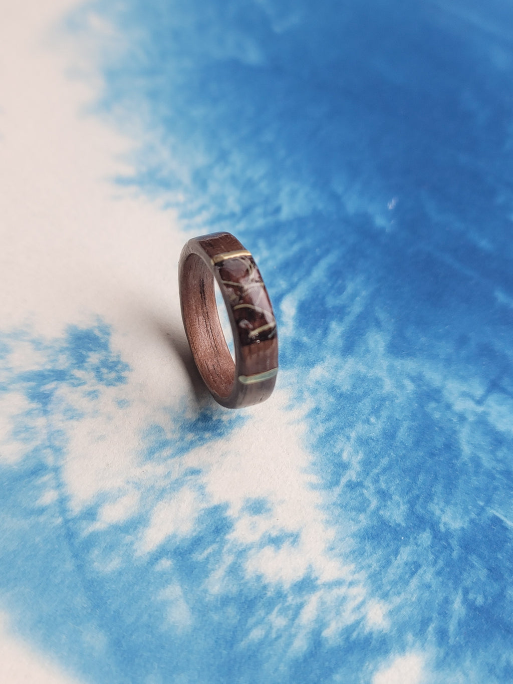 Wooden ring with metal accents on a blue and white cloud background