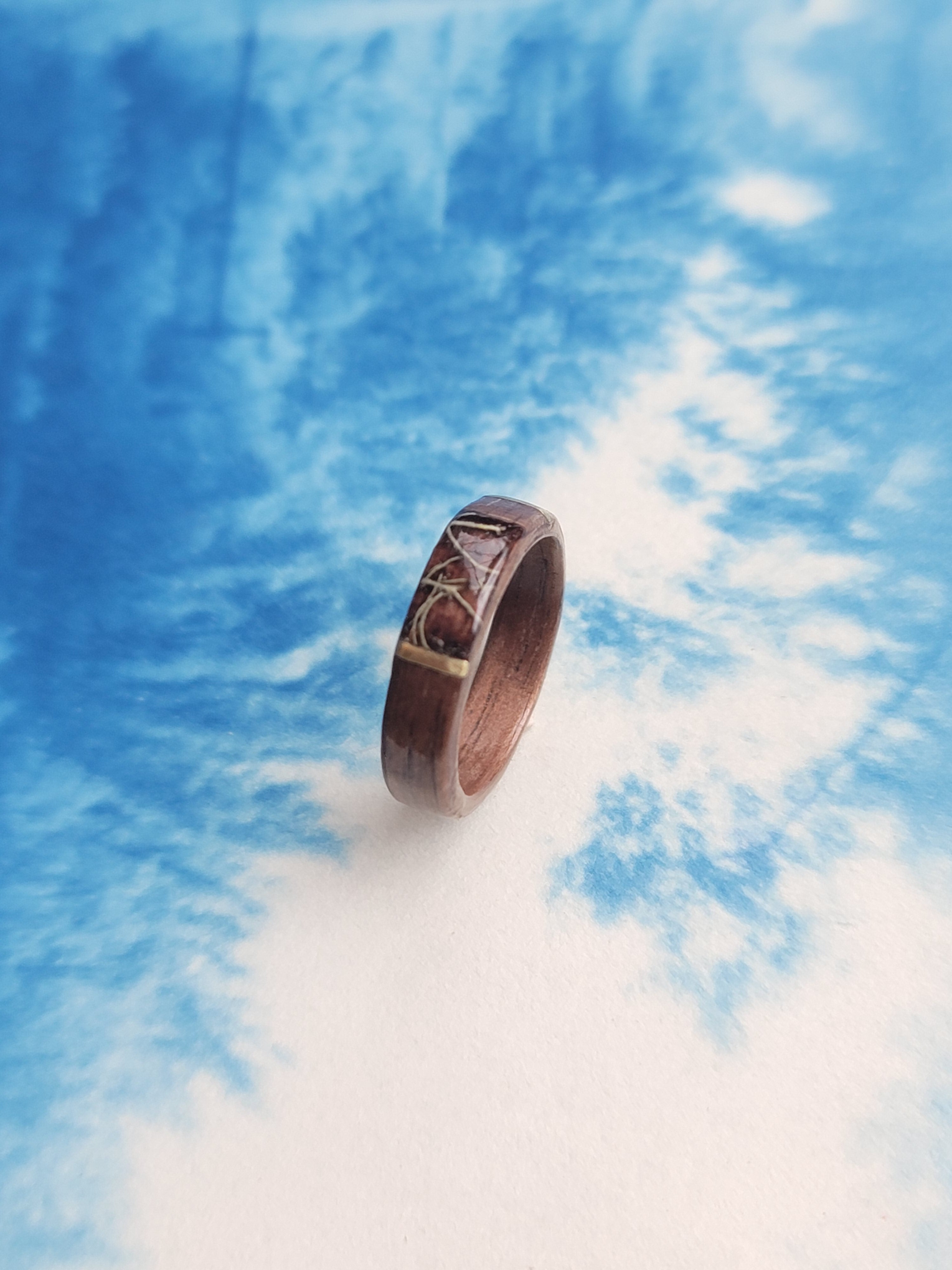 Wooden ring with metal accents on a blue and white cloud background