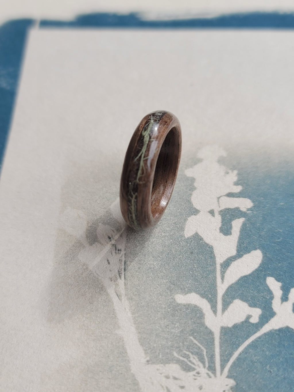 Wooden ring with embedded Lichen on a textured white surface