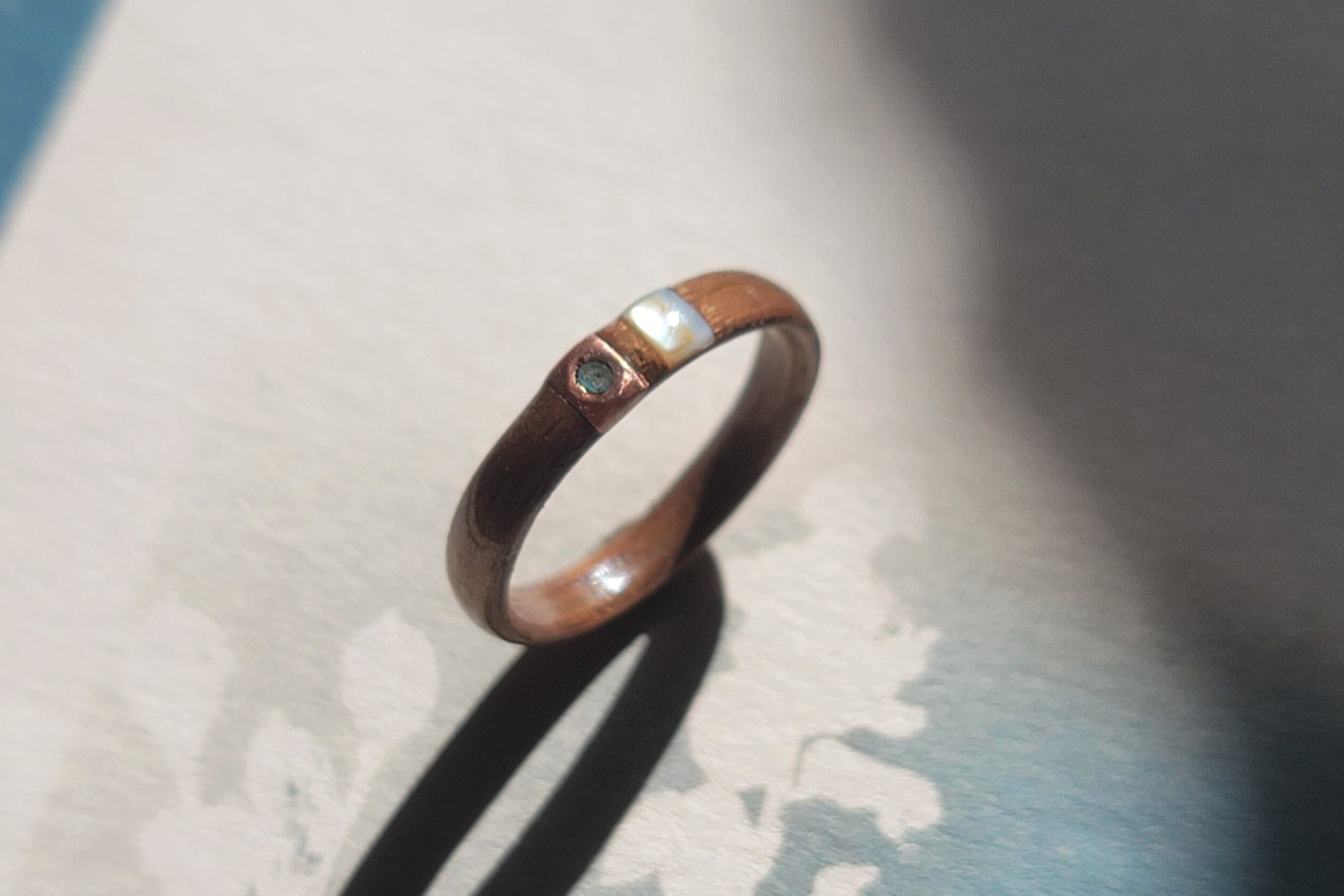 Wooden ring with copper and mother of pearl inlays on a textured background
