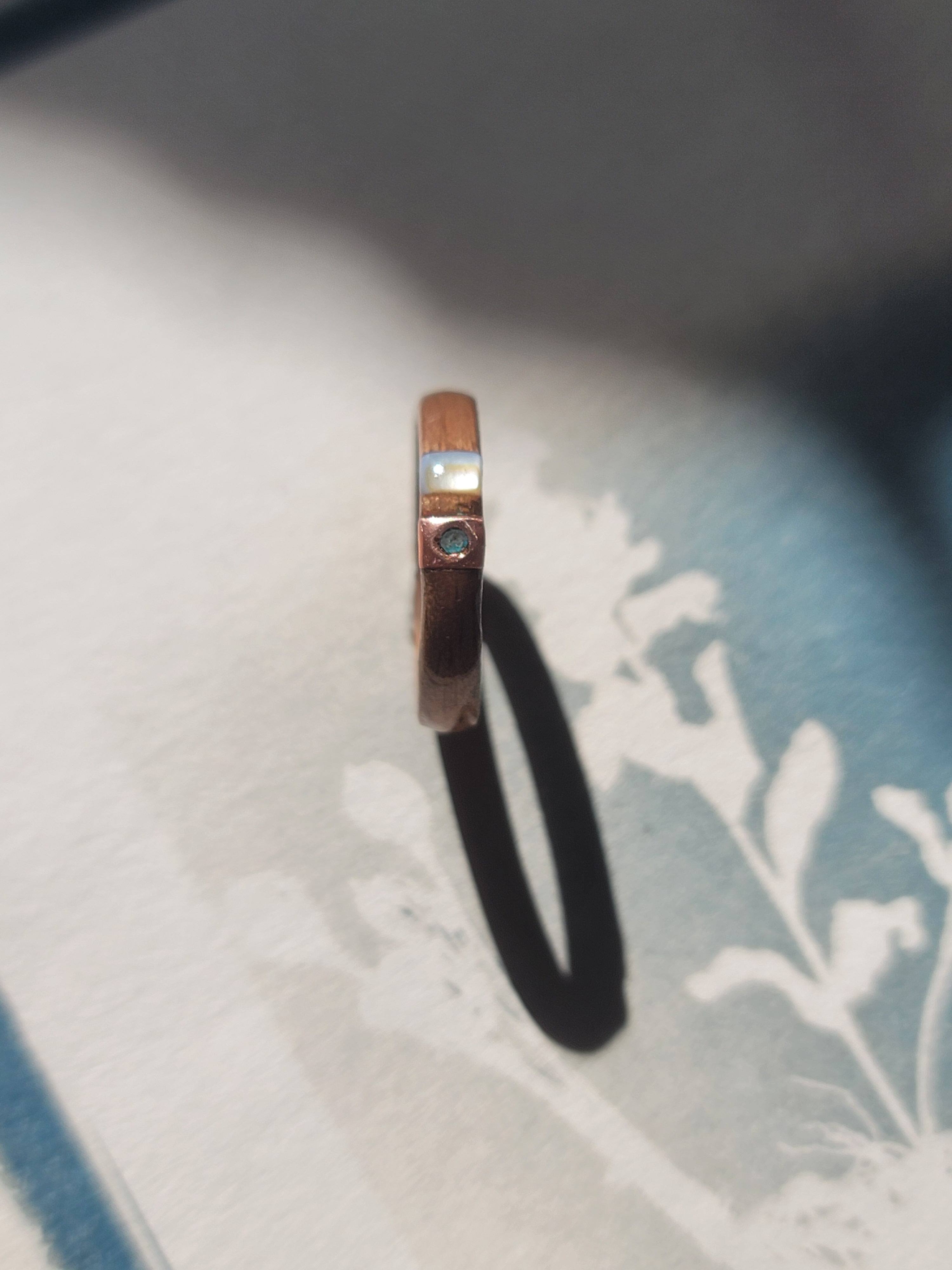 Wooden ring with copper and green verdigris on a white fabric background