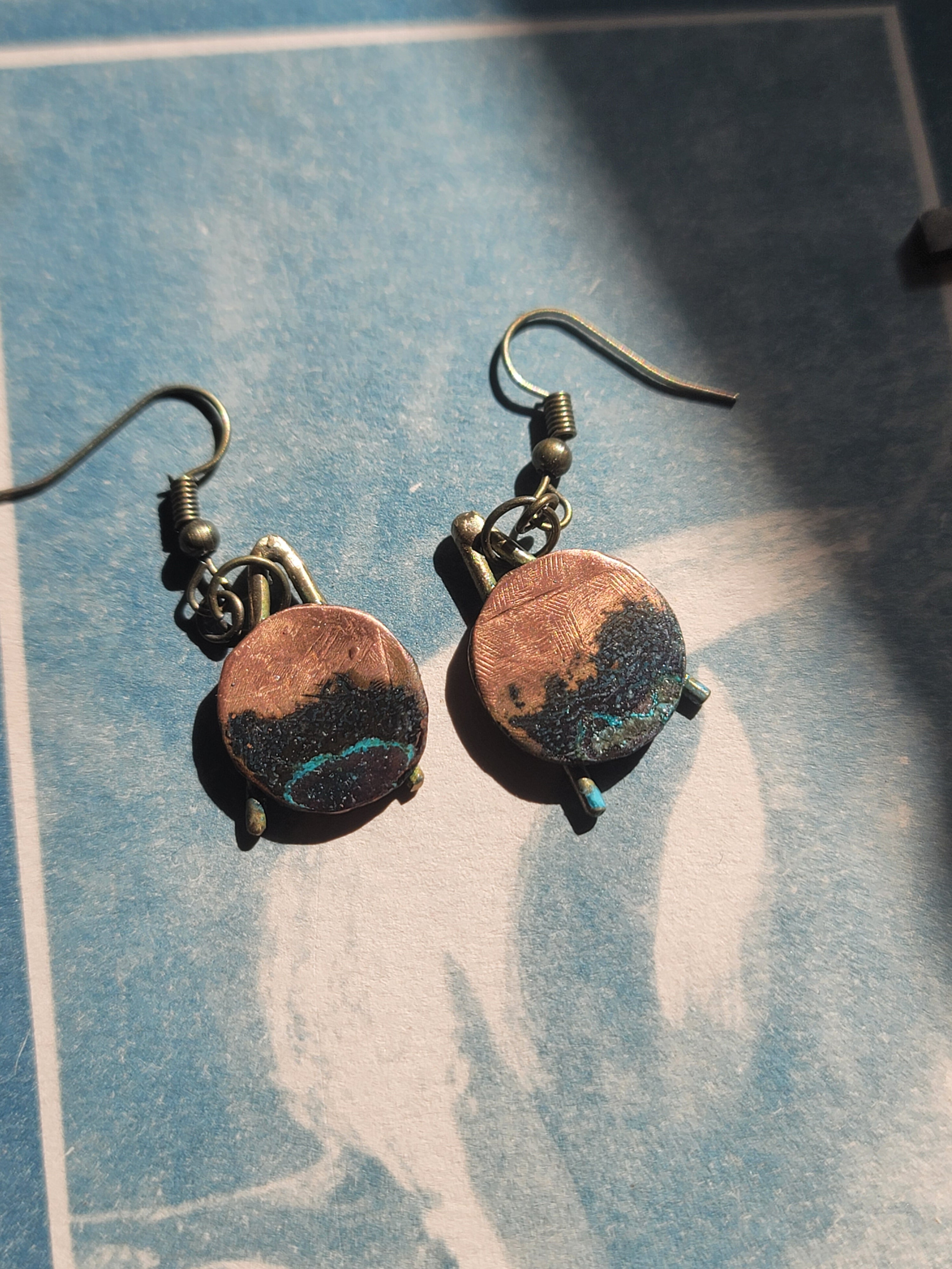 Pair of earrings with circular designs on a textured blue surface