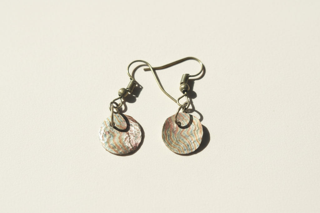 Pair of earrings with shell-like designs on a textured surface