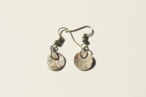 Pair of earrings with shell-like designs on a textured surface