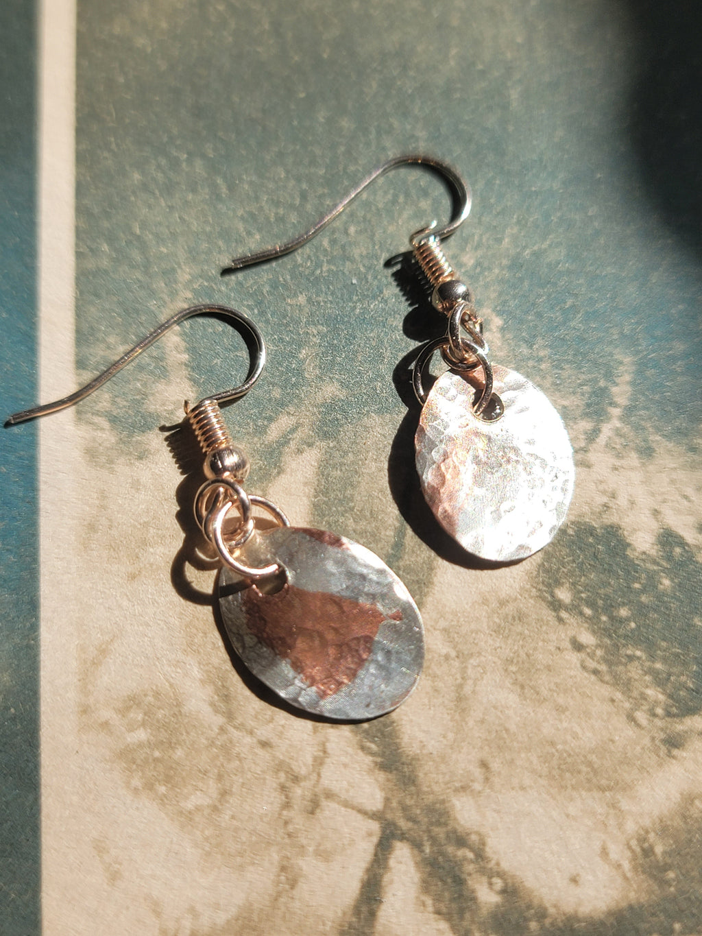 Pair of silver and copper earrings on a textured surface
